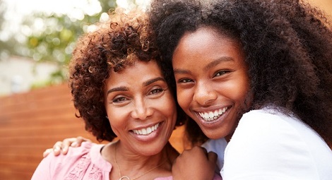 Young woman embracing an older woman.  Both facing the camera and smiling